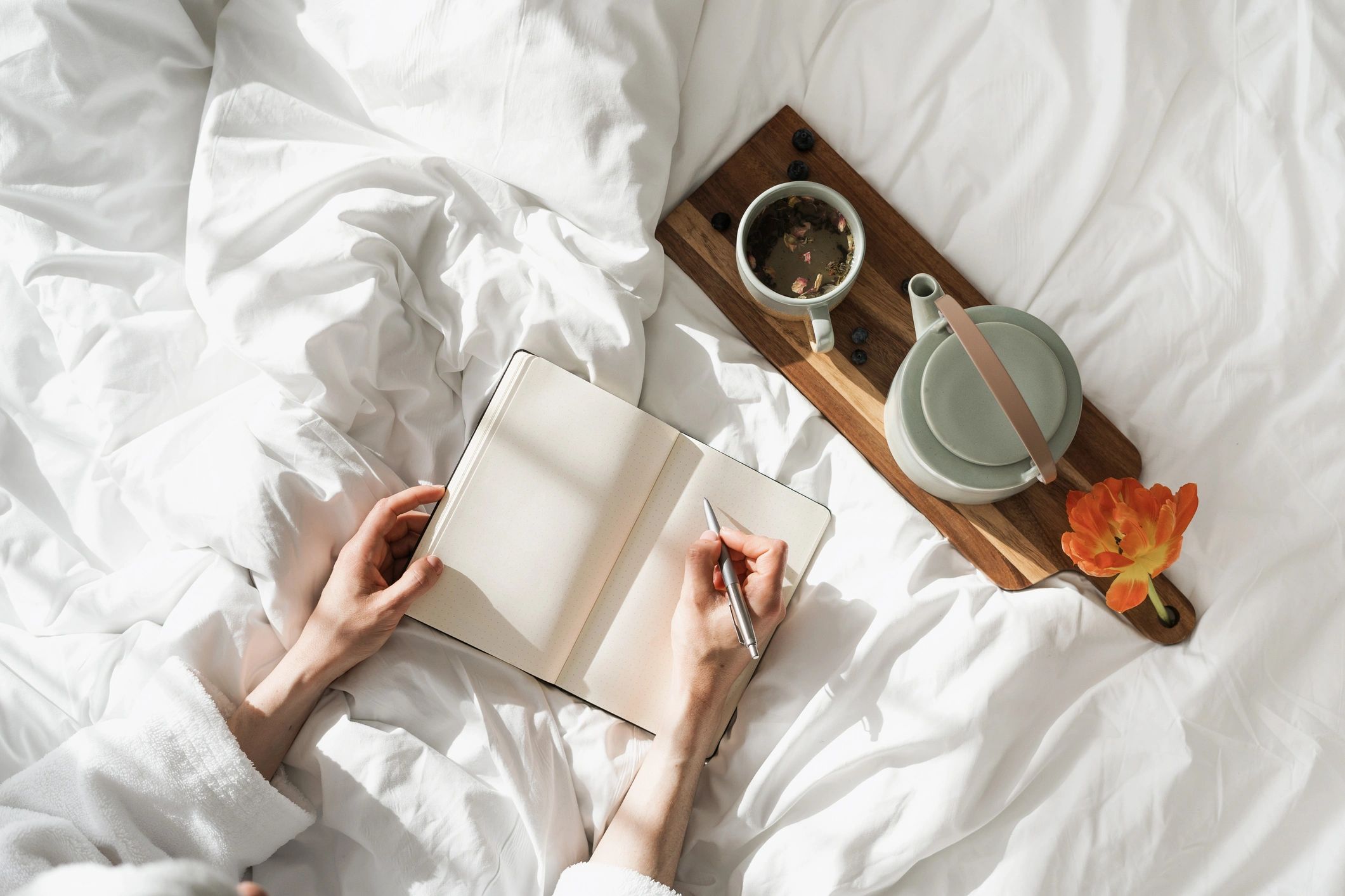 Person writing notes in a notebook while sitting in bed